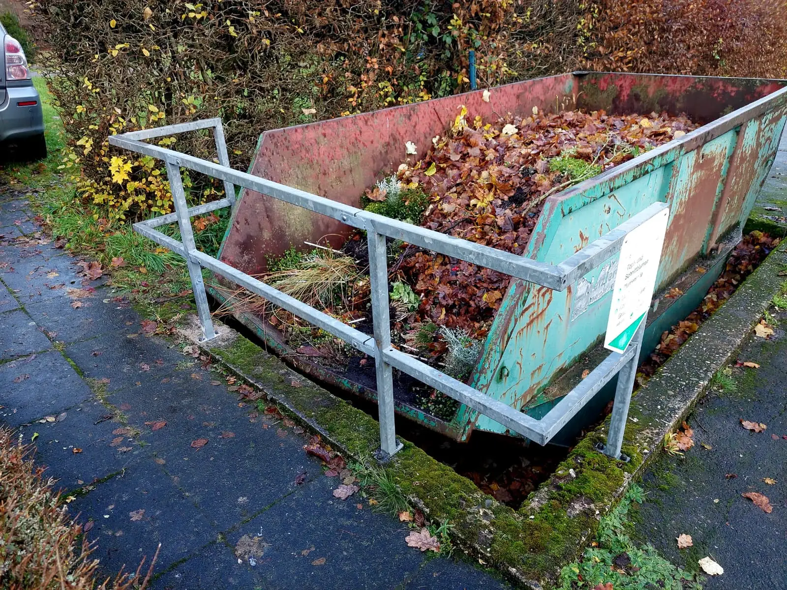Verzinktes Schutzgeländer entlang einer abgesenkten Containerbucht für Grünabfall auf einem Friedhof