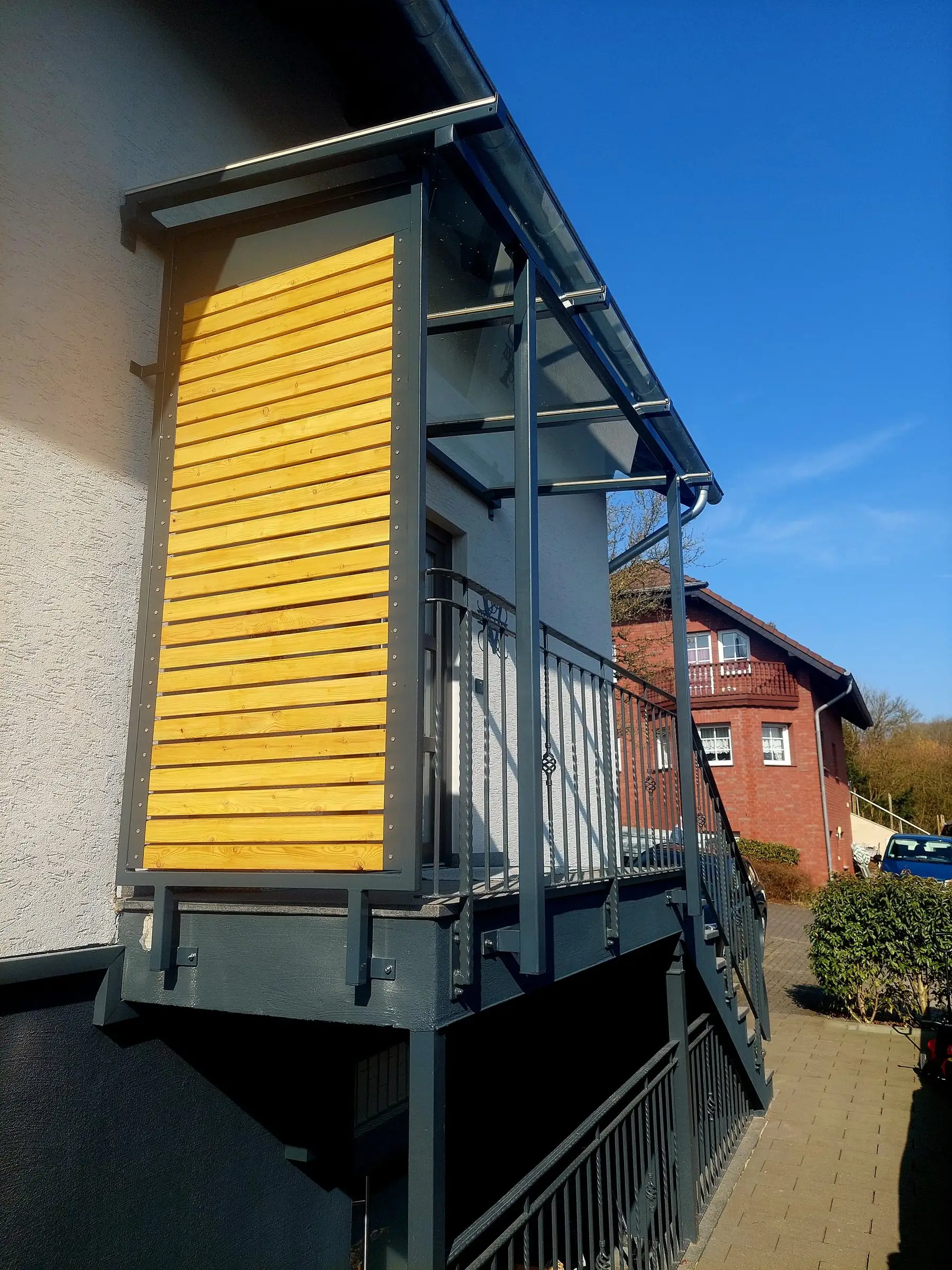 Erhöhtes Stahlpodest mit Geländer, Seitenwand aus Holz und Treppe an einer verputzten Fassade