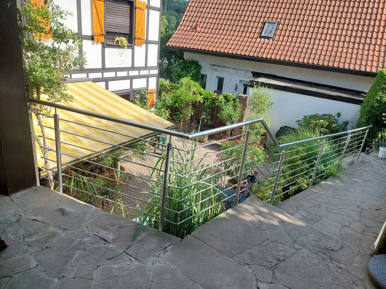 Edelstahlgeländer an einer Außentreppe neben einem Fachwerkhaus, an den schiefen Bestand angepasst