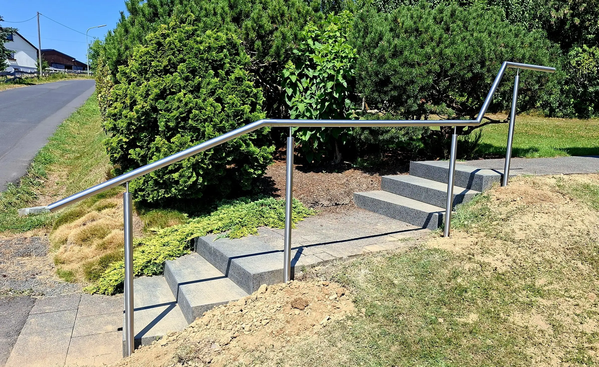Durchgehender Edelstahlhandlauf auf Rundpfosten entlang einer Granittreppe mit zwei Läufen im Garten