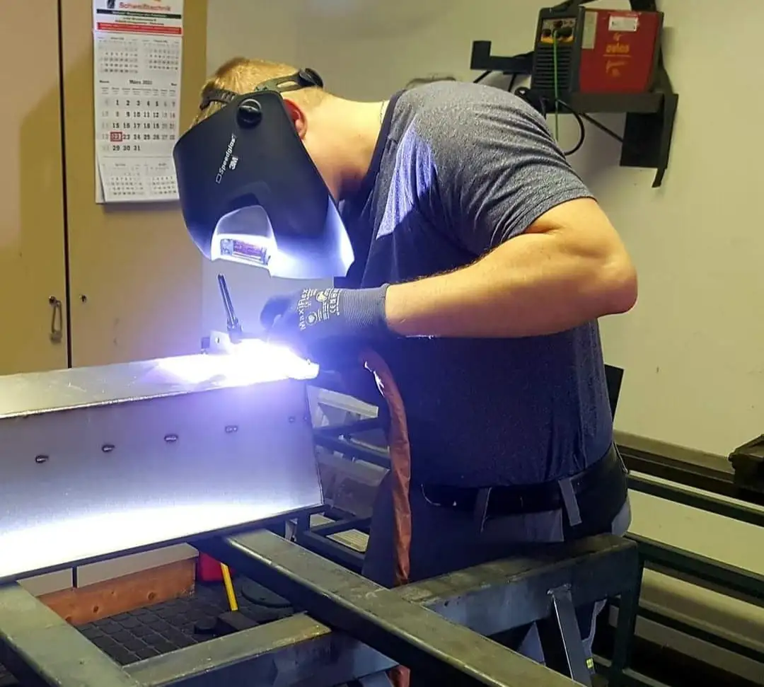 Alexander Blaschke schweißt in seiner Werkstatt an einem Stahlträger, heller Lichtbogen unter dem Schweißhelm