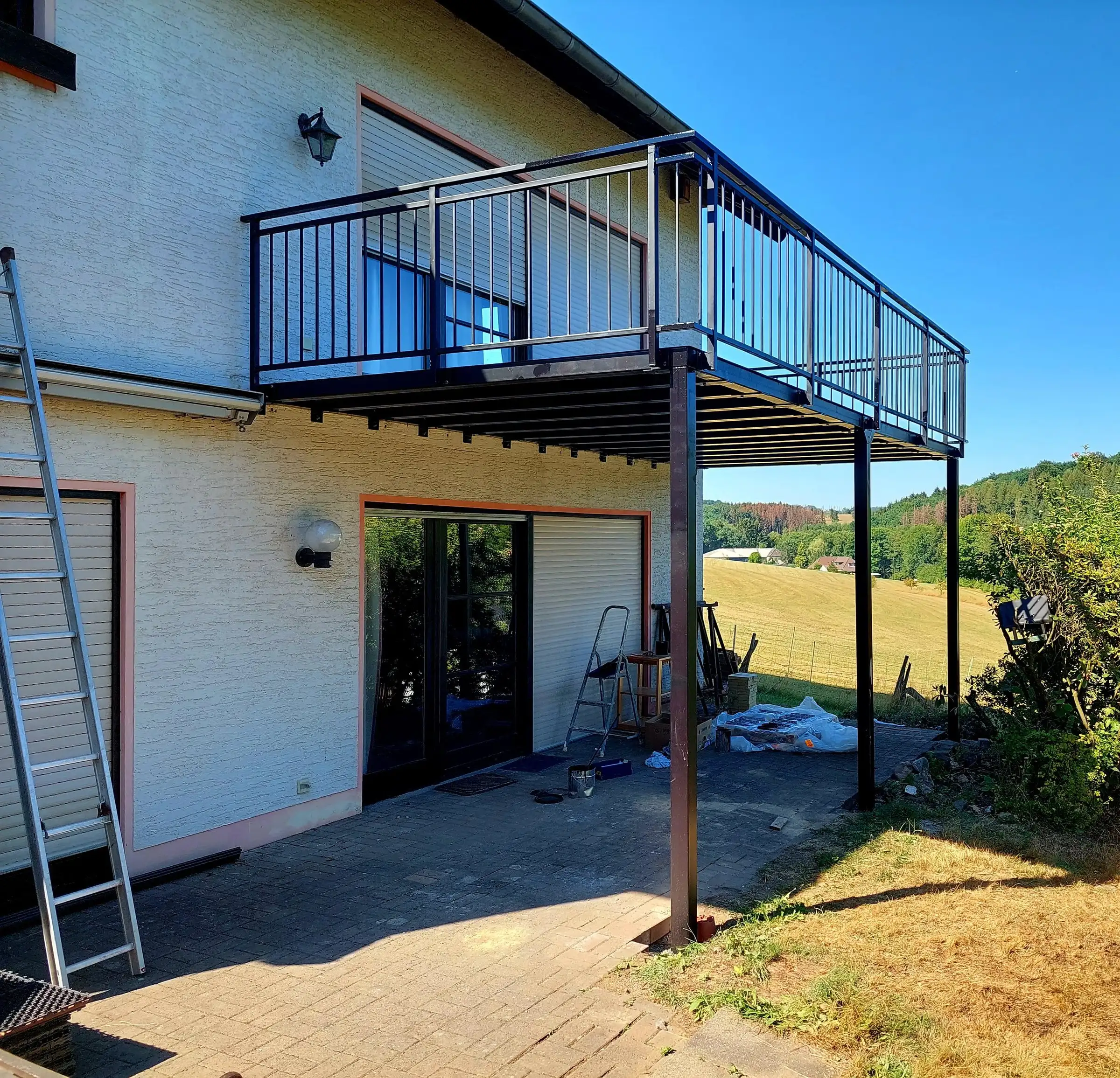 Angebauter Stahlbalkon auf Stützen mit umlaufendem Geländer an der Rückseite eines Wohnhauses