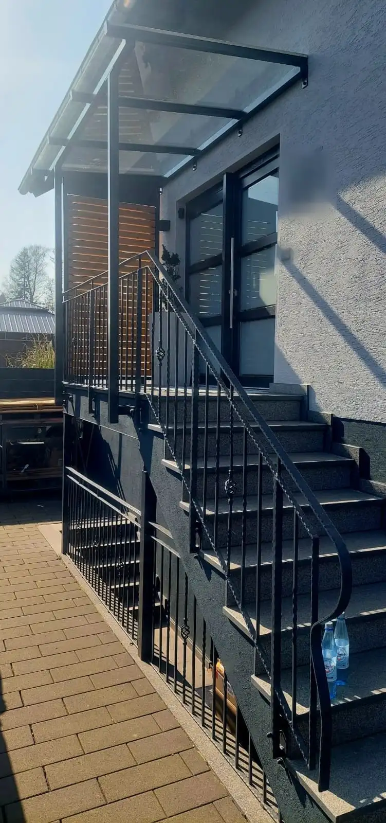 Stahlkonstruktion eines Eingangspodests mit Treppe, Geländer und Glasvordach an einem Wohnhaus