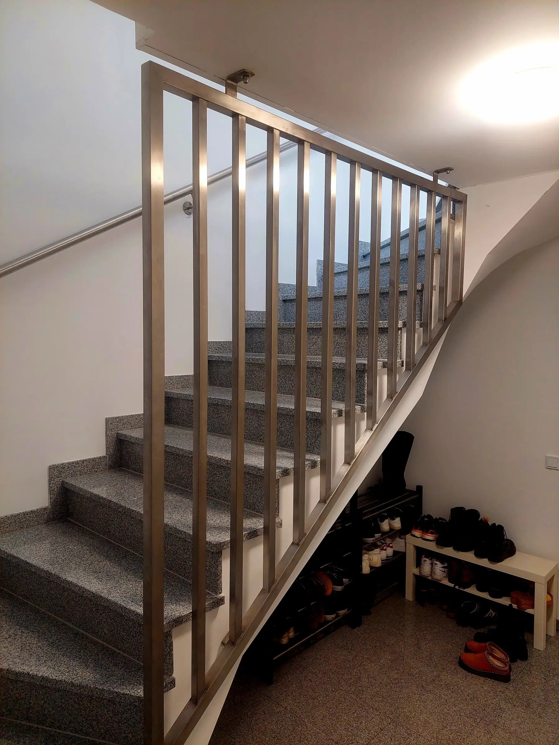 Geländer aus Edelstahl-Vierkantrohr mit senkrechten Stäben an einer Granittreppe im Treppenhaus